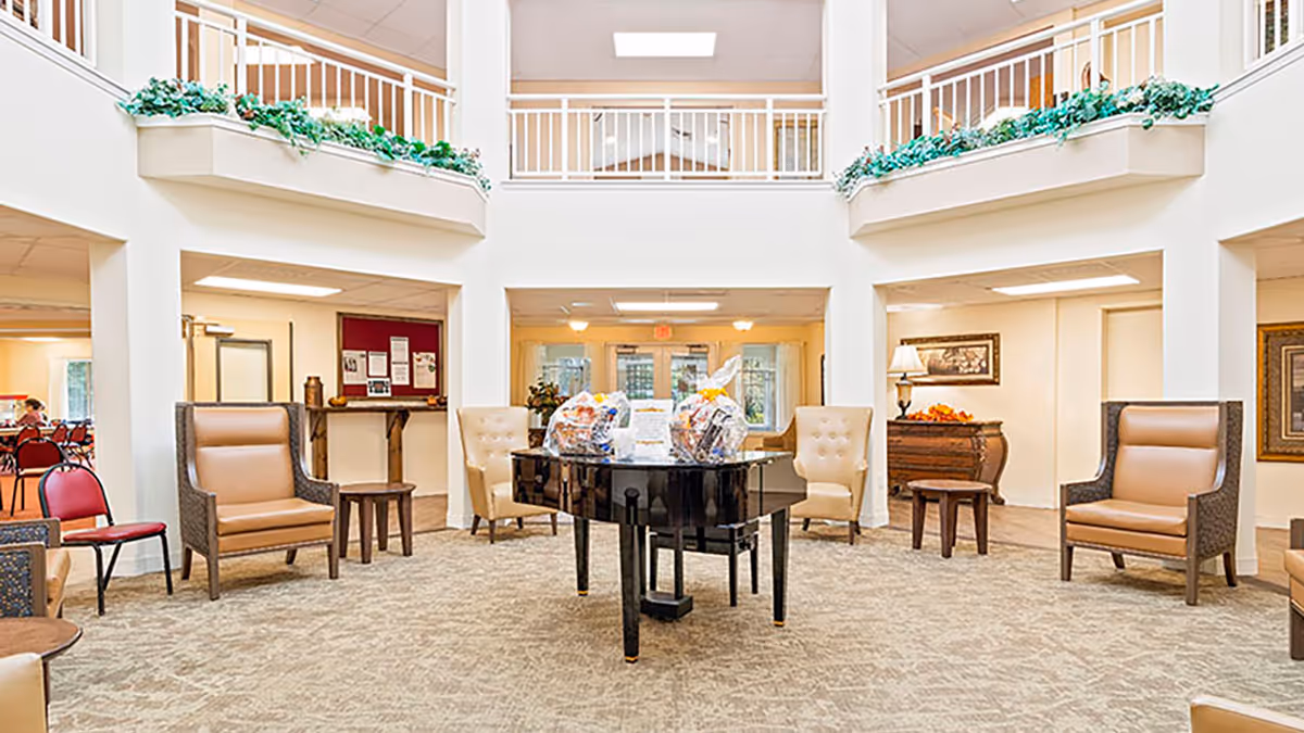 Bright two-story common lobby with a grand piano at the center surrounded by armchairs and seating.