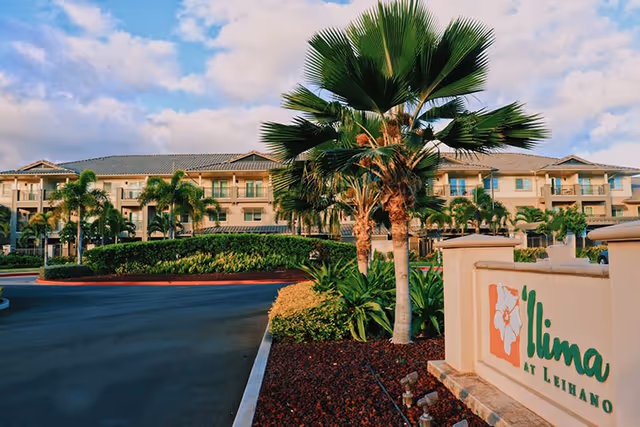Exterior front view of the Ilima at Leihano building with palm trees, landscaping, driveway, and an entrance sign.