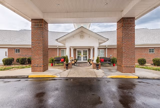 Covered entrance to a brick building with large columns, benches, and potted plants.