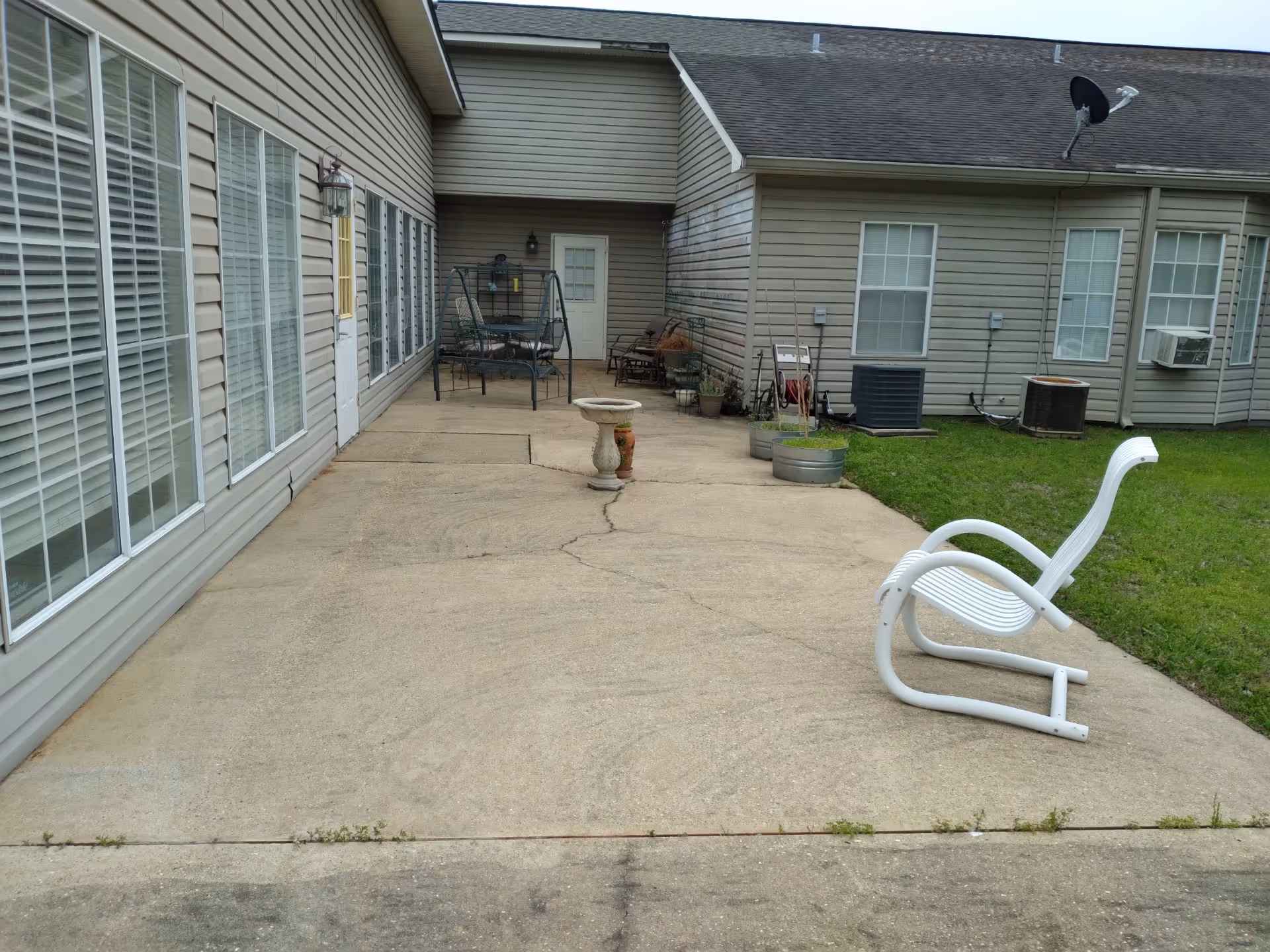 Concrete courtyard patio beside a single-story building with windows, outdoor chairs, a swing, and potted plants.