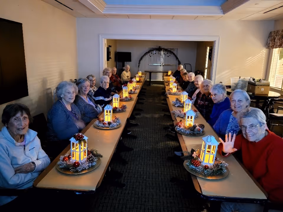 Residents sit along a long table in a dimly lit community dining room with illuminated decorative lantern centerpieces.