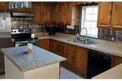 Kitchen with wood cabinets, a small central island, stainless steel appliances, a sink under a window, and patterned backsplash tiles.