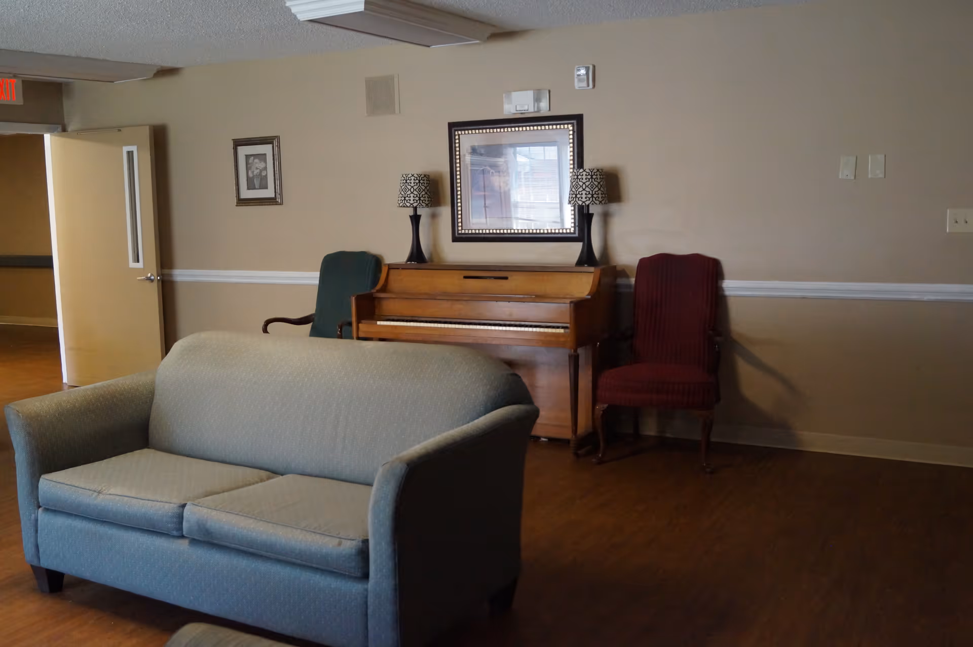 Sitting area with a couch in the foreground and an upright piano against the wall flanked by chairs and lamps.