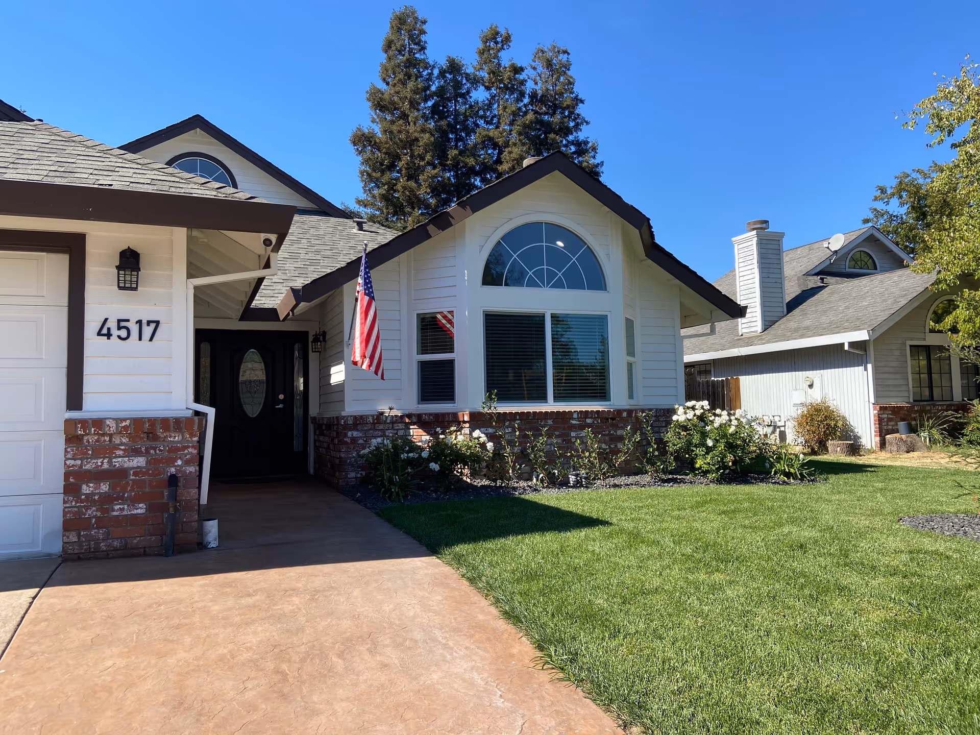 Front exterior of a single-story house with an arched window, brick trim, American flag, and address number 4517.