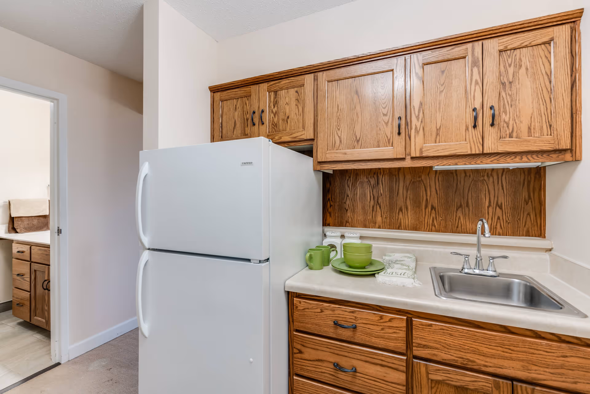 Compact kitchen with a white refrigerator, oak cabinets, a countertop sink, and green dishware.