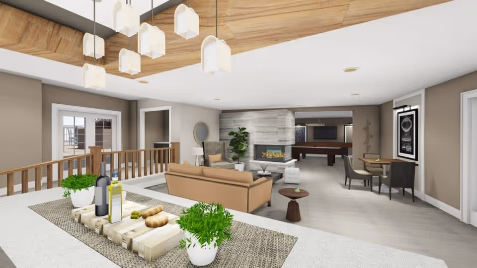 A spacious and modern living room area with a beige sofa, armchair, and coffee table in front of a contemporary fireplace. There is a dining table with chairs on the right side and a pool table in the background. The ceiling features wooden paneling and hanging pendant lights. A countertop in the foreground has decorative plants, bottles, and bread on a wooden tray.