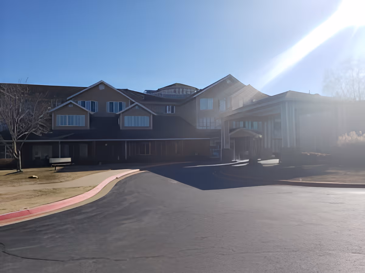 Front exterior of a multi-story senior living building with a covered entrance and driveway under bright sunlight.