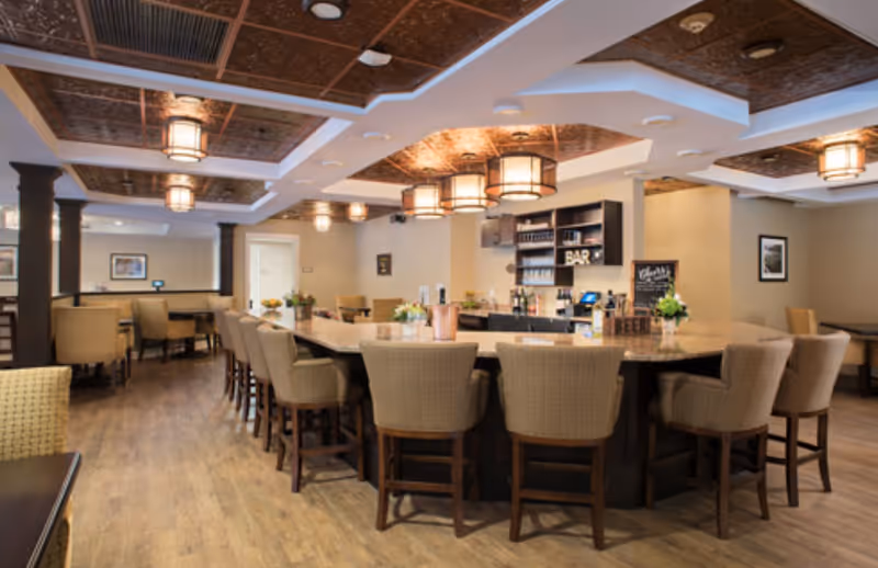 Spacious dining/lounge area with a central bar surrounded by upholstered bar stools and pendant lights.