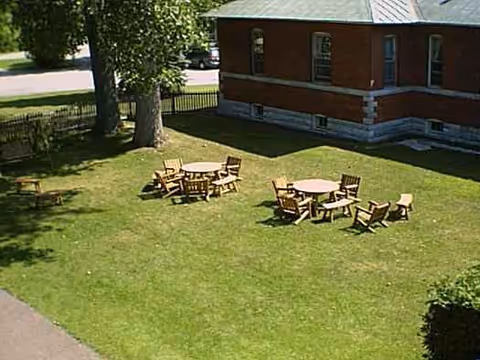 Outdoor grassy courtyard with wooden tables and chairs beside a brick nursing building.