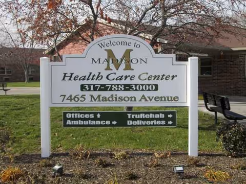 A large sign reading Welcome to Madison Health Care Center in front of a brick building.