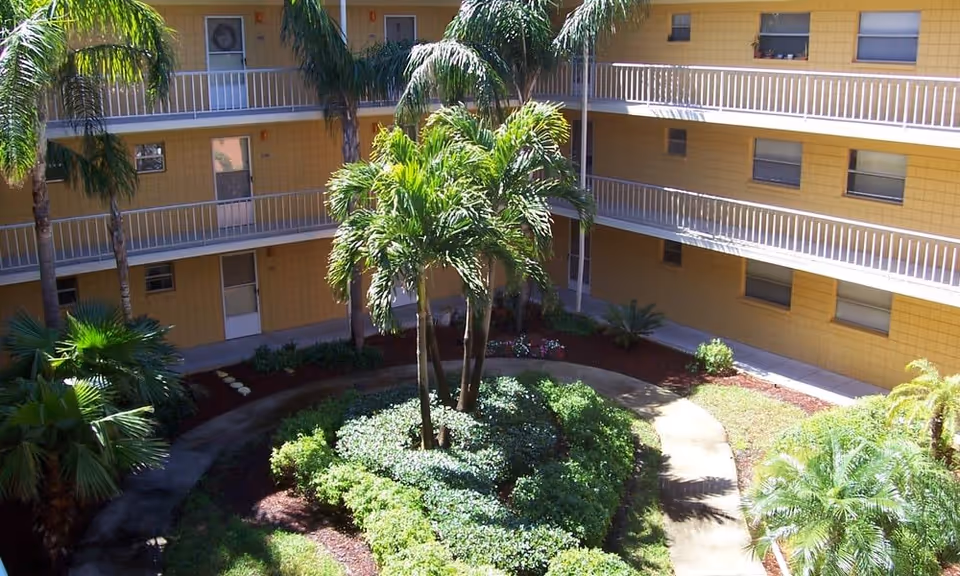 Central courtyard of a yellow three-story apartment building with palm trees and walkways.