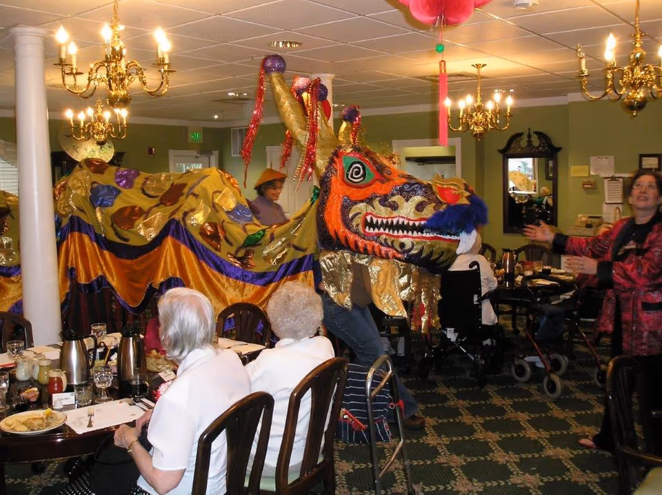 Residents watch a colorful Chinese dragon costume performing in a dining room.