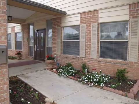 Exterior view of a brick senior living facility with a front entrance and flower beds.