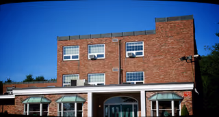 Brick building with arched entrance and green awnings, front view of a senior care center.