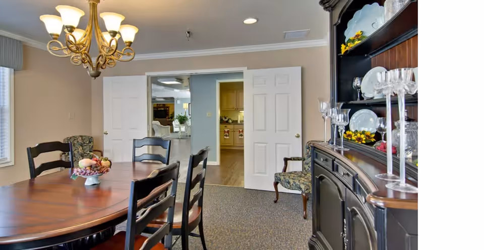 Dining room featuring a wooden oval table with chairs under a chandelier, a china cabinet on the right, and open double doors leading to adjacent rooms.