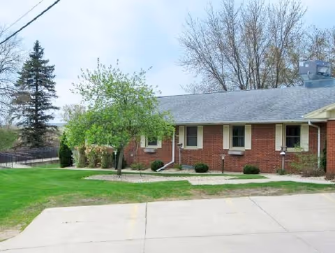 Brick single-story Good Samaritan Society building with walkway, trees, and manicured landscaping.