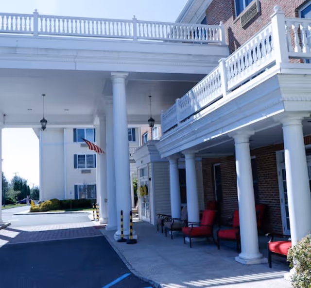 Covered front entrance with white columns, balcony railings, red chairs and an American flag.