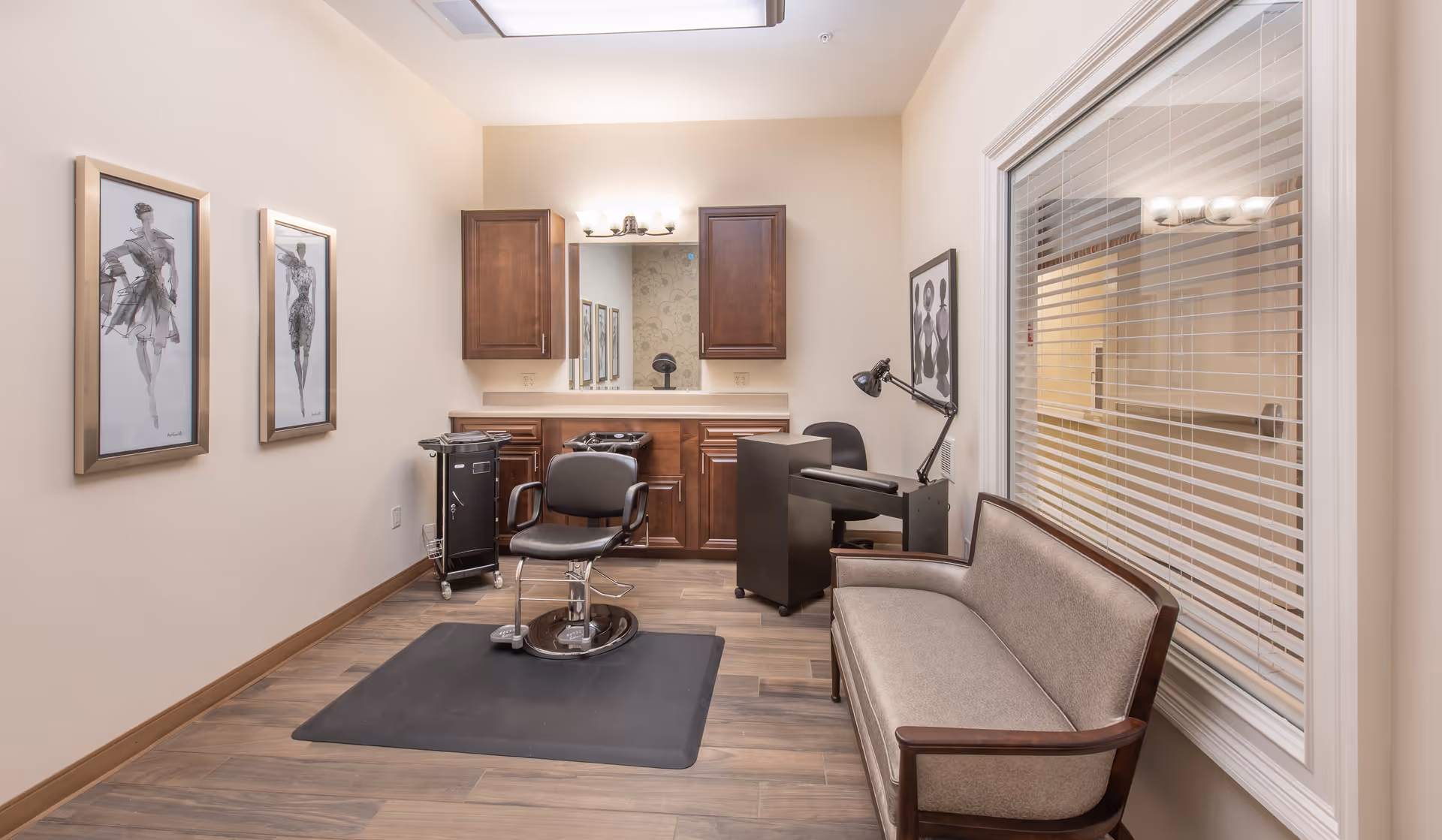 Small salon-style interior with a styling chair on a mat, cabinets and mirror, a couch and framed artwork.