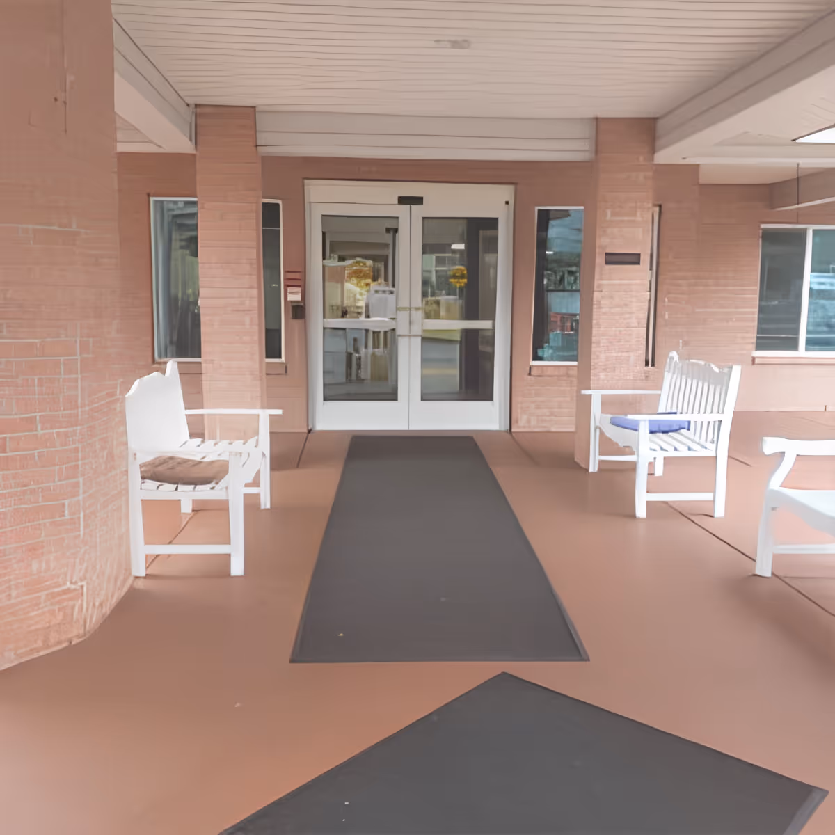 Covered entryway with glass double doors and white chairs on either side of a walkway.