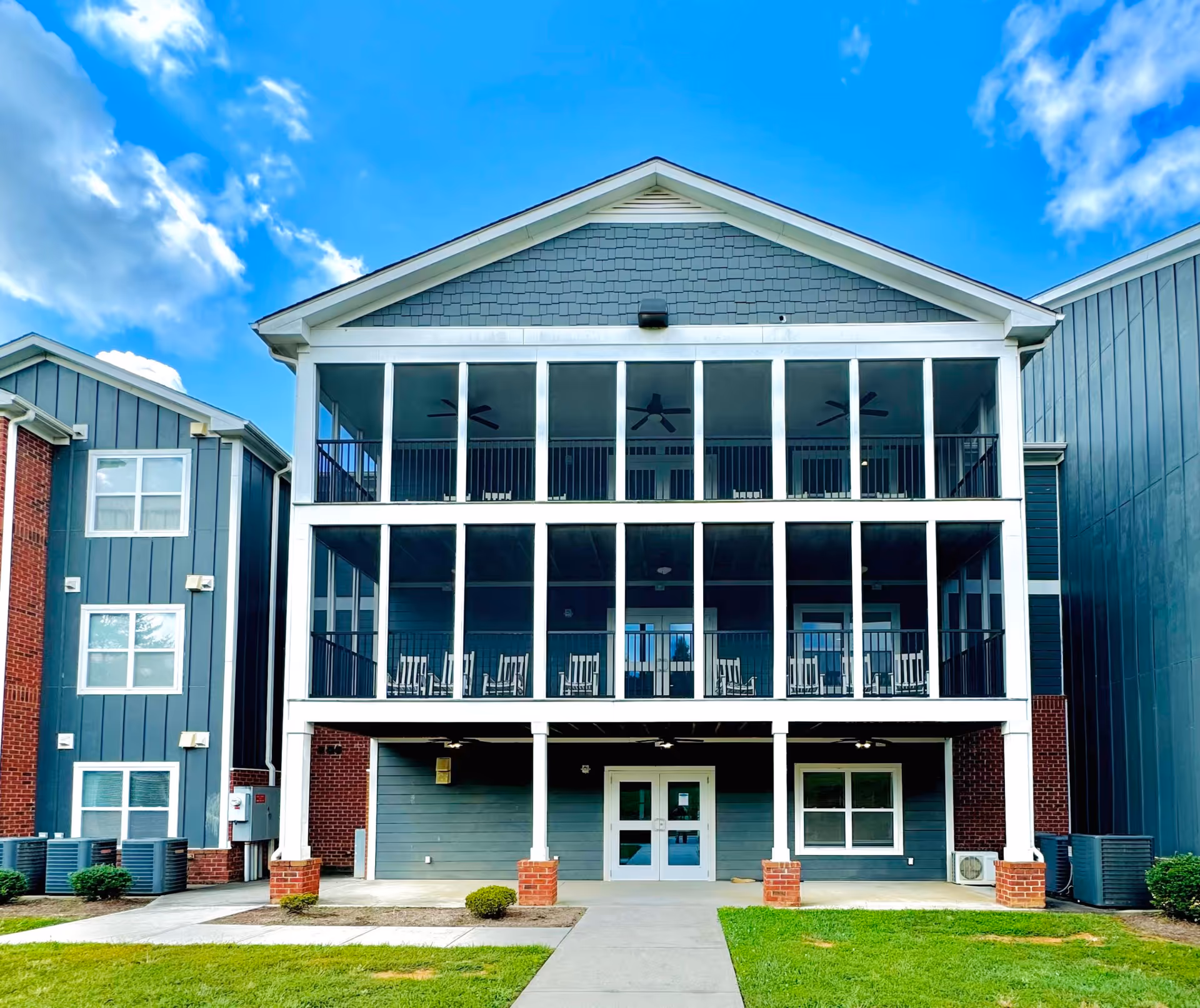 Front exterior of a three-story residential building featuring stacked screened balconies above a ground-level entrance.