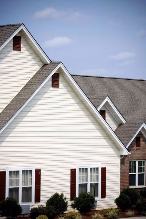 Exterior view of a cream-colored senior living building with peaked roofs and red shutters.
