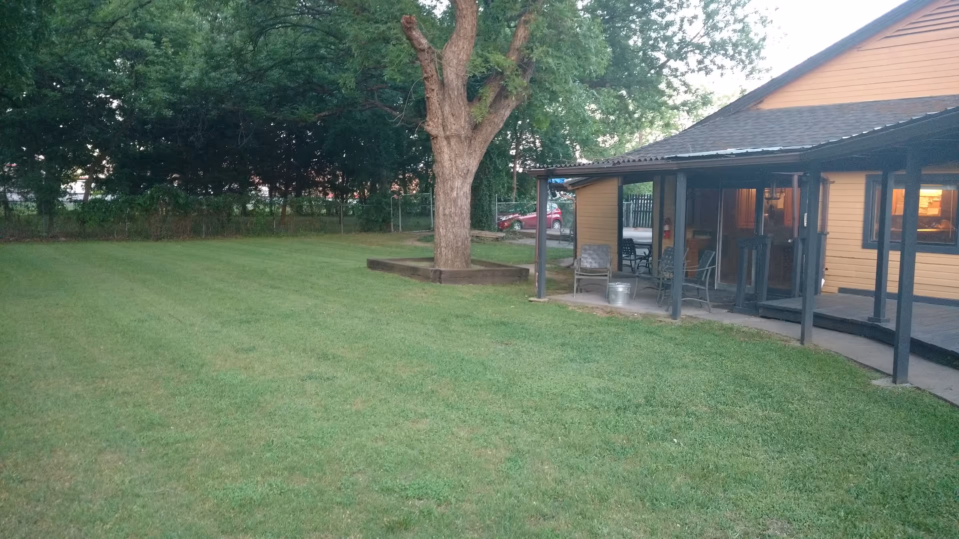 Grassy yard with a large tree and a covered porch attached to a yellow building.