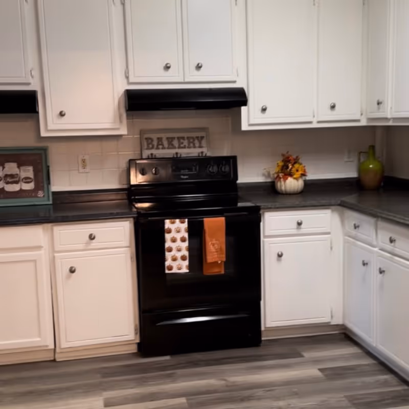 Kitchen with a black stove flanked by white cabinets, dark countertops, and decorative accents including a 'Bakery' sign and seasonal decor.