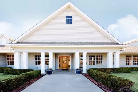 Front exterior view of a light-colored senior living building with columns and a wooden door.