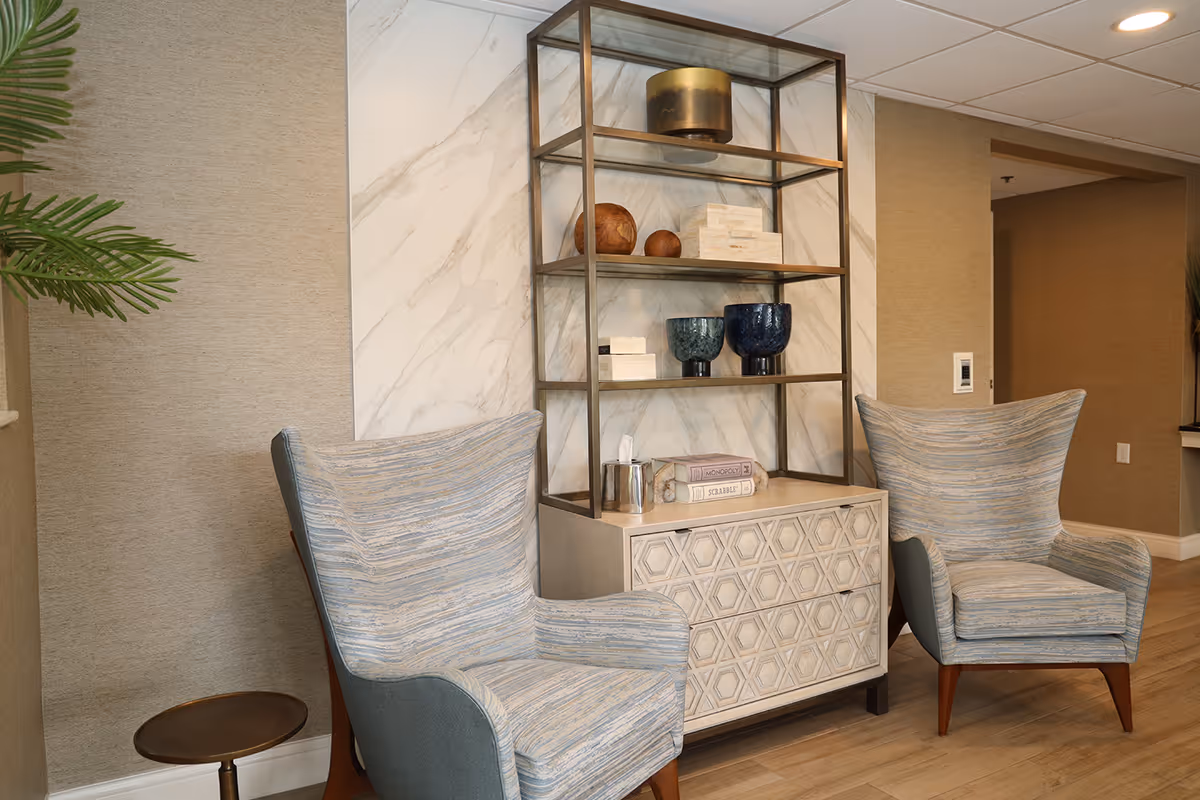 Two upholstered armchairs flank a decorative shelving unit and cabinet in a cozy sitting area.