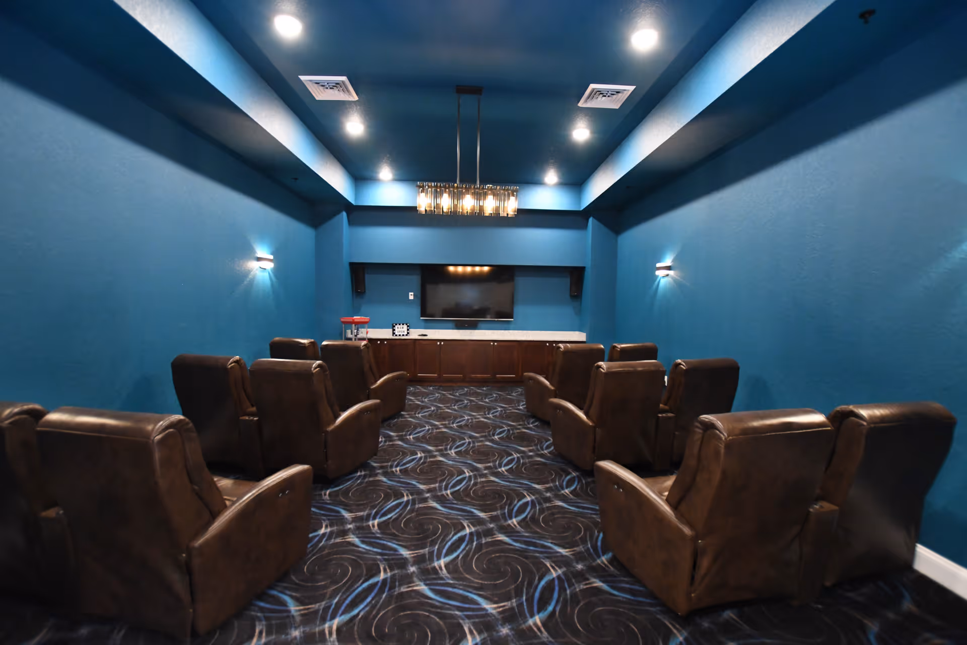 Small private theater room with leather recliner chairs facing a wall-mounted TV in a blue-painted room.