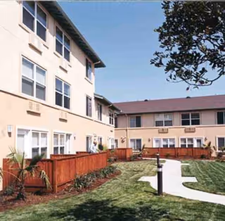 Exterior of a two-story senior living building with a grassy courtyard and wooden fences.