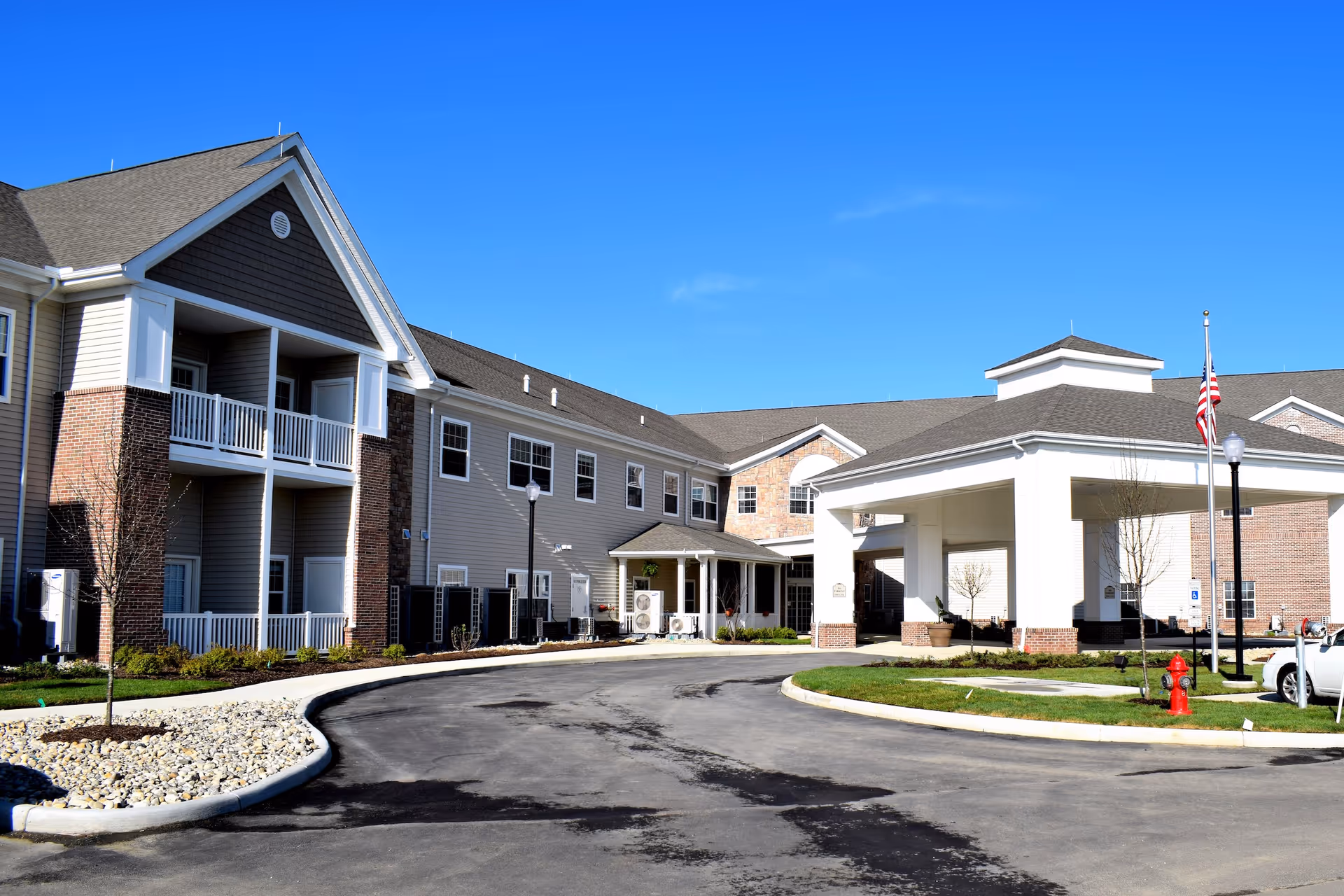 Exterior view of Danbury Huber Heights senior living facility with driveway, entrance, and flag.