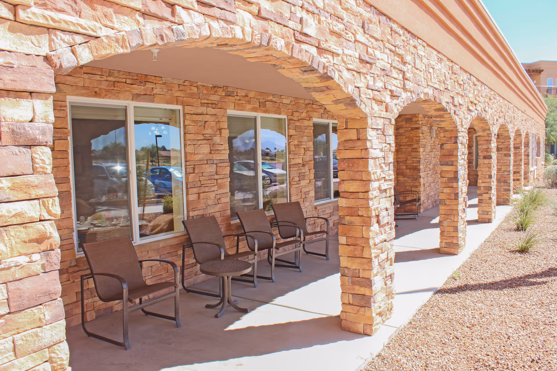 Stone-arched covered patio with several chairs and small tables along the front of a senior living building.