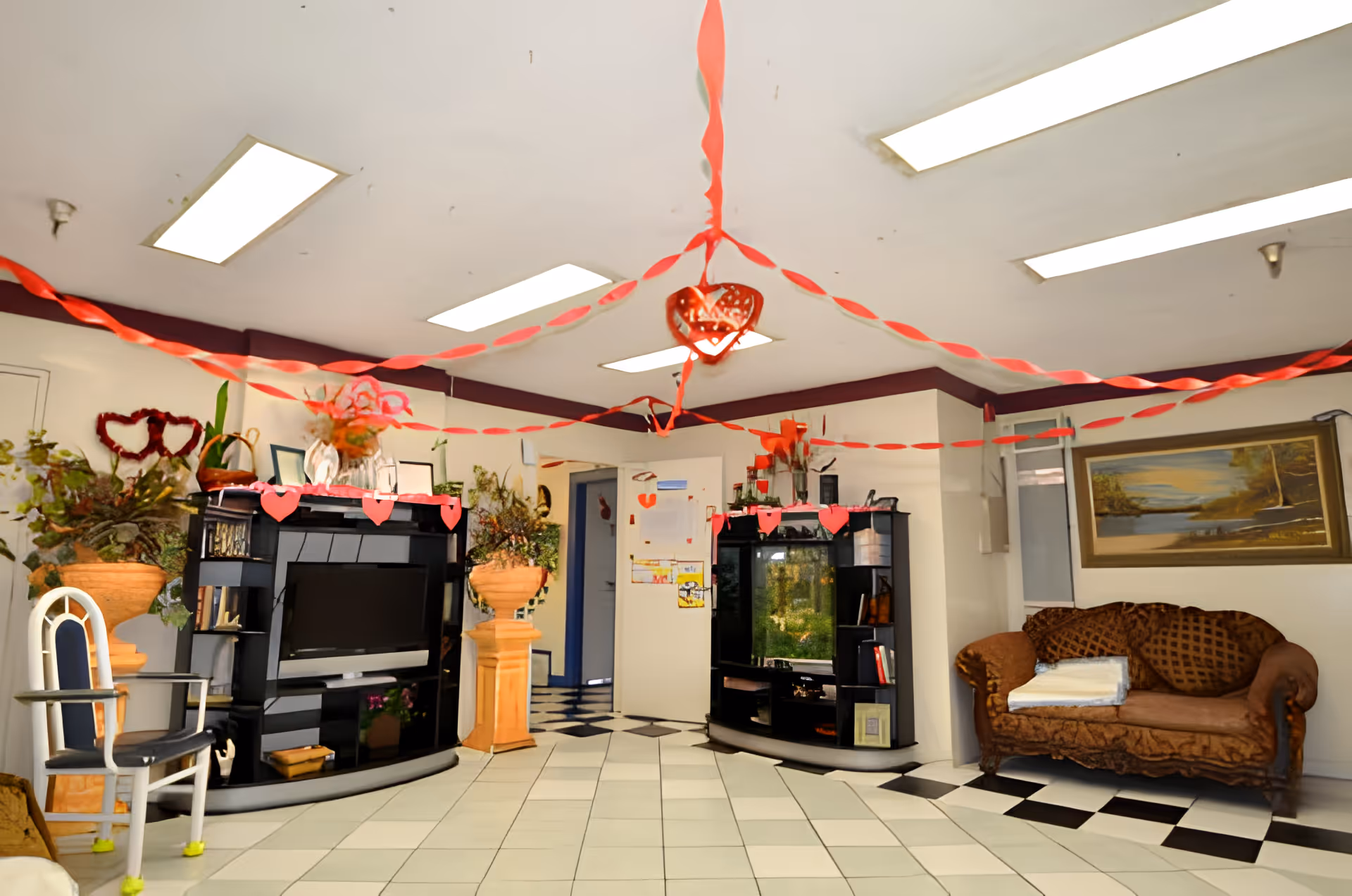 Community lounge with TV cabinets, potted plants, a couch, and red Valentine decorations hanging from the ceiling.