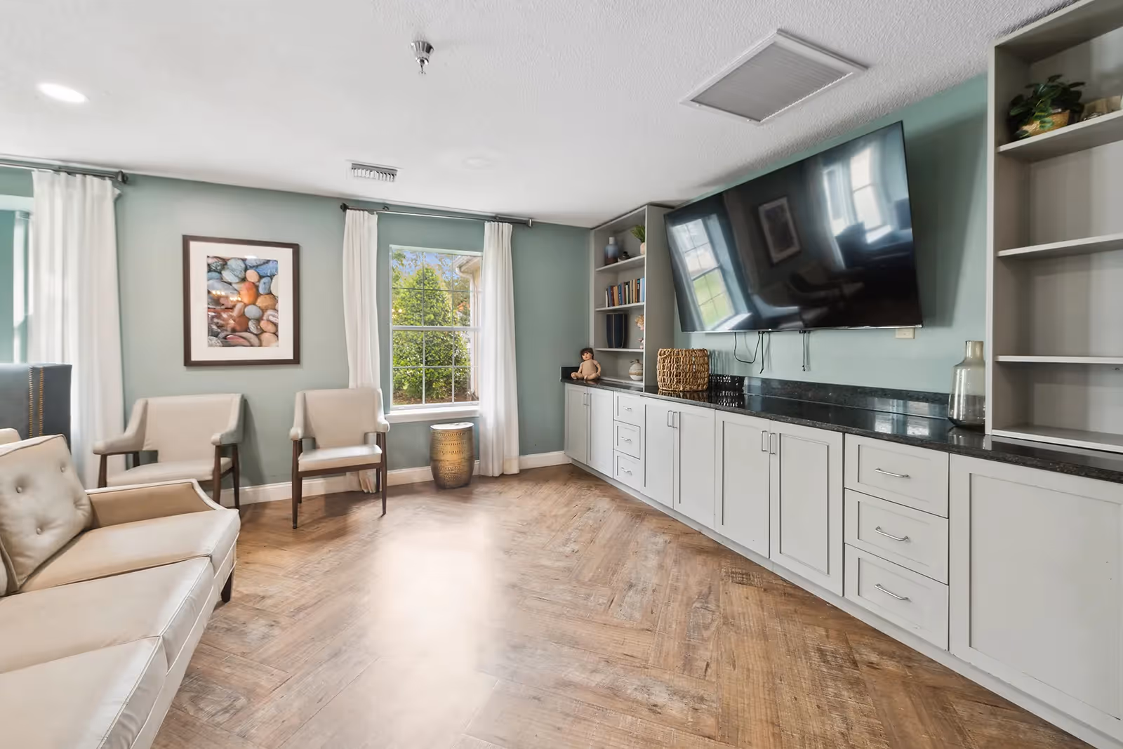 Light-filled seating area with armchairs, a sofa, built-in cabinets and a large wall-mounted TV.
