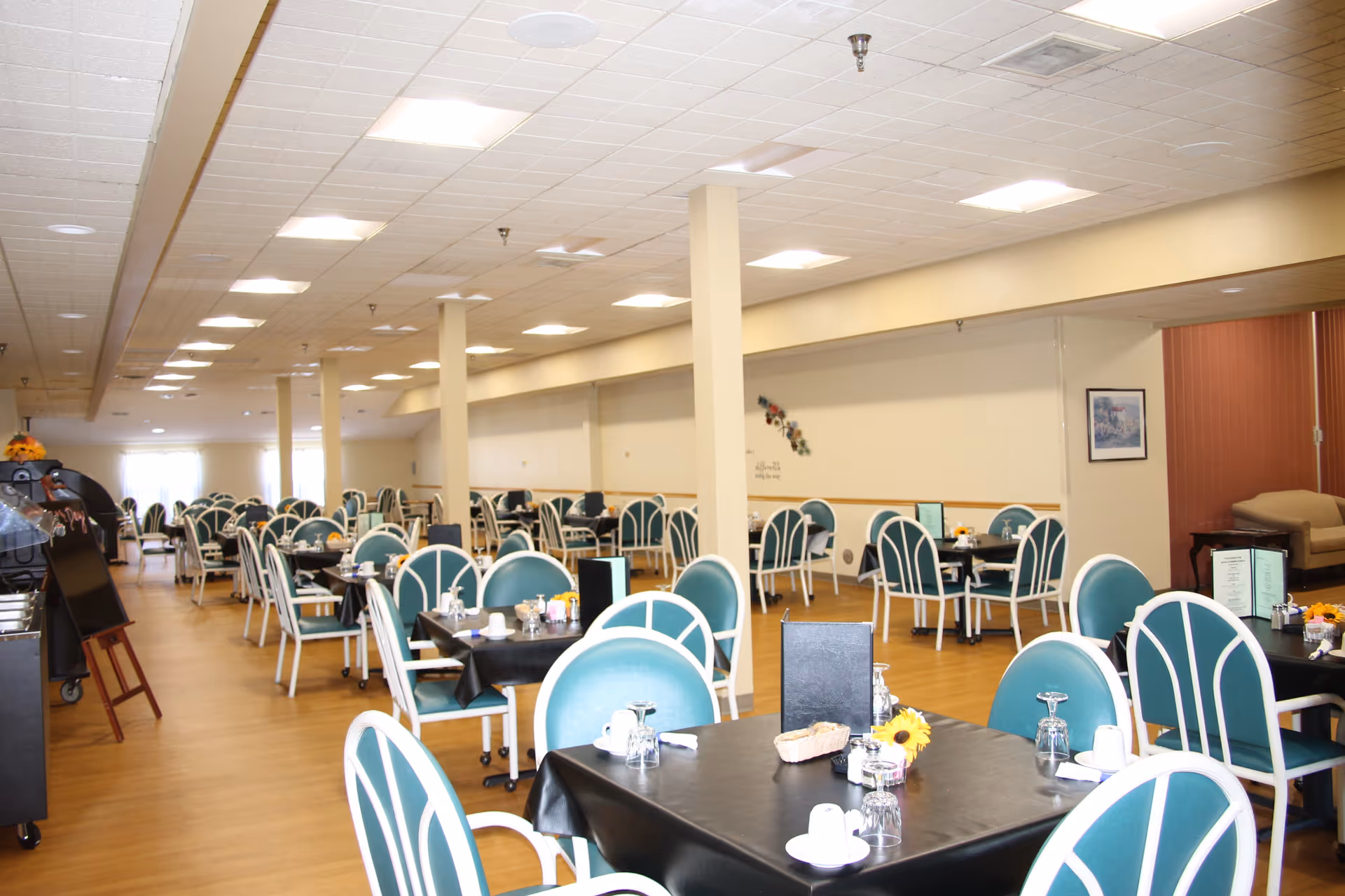 Large communal dining room with rows of tables and teal-backed chairs set for meals.