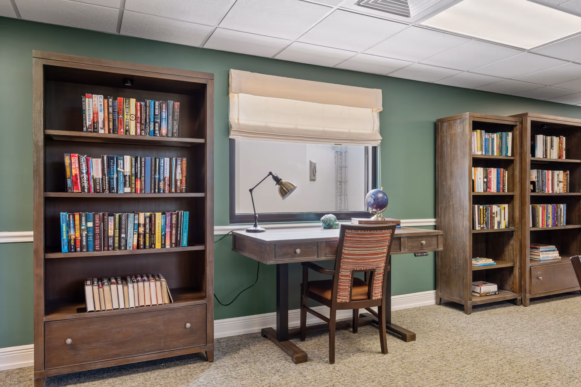 A cozy interior reading area with wooden bookshelves flanking a desk and chair beneath a window, holding books and a globe.