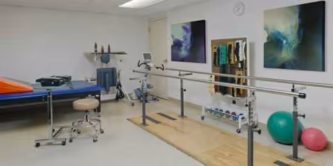 Rehabilitation therapy room with parallel bars, mats, and assorted exercise equipment.