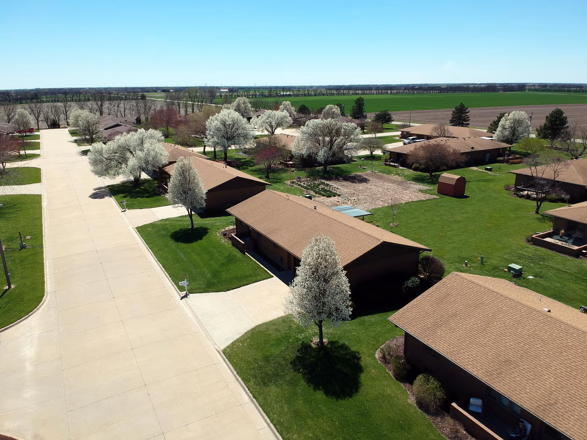 Aerial view of a campus of single-story residences with tree-lined lawns, driveways, and paved roads.