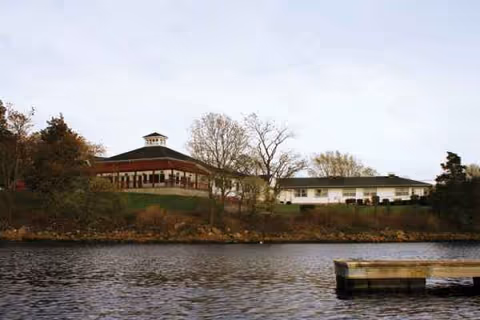 Exterior view of a single-story senior care building by a lake with a wooden dock.