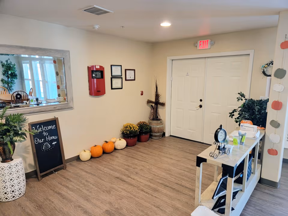 Entrance lobby of a senior living home with autumn decorations including pumpkins, a welcome chalkboard, plants and a small console table.