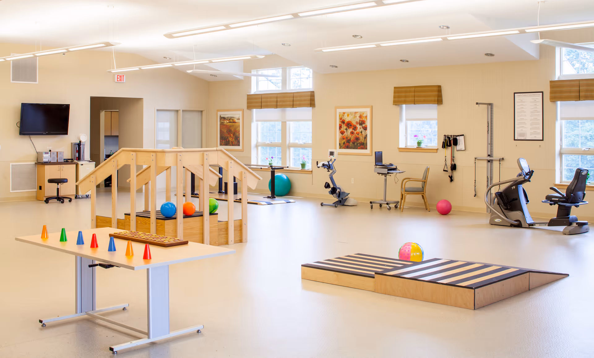 Bright, spacious rehabilitation and exercise room with therapy equipment, ramps, balls, and activity tables.