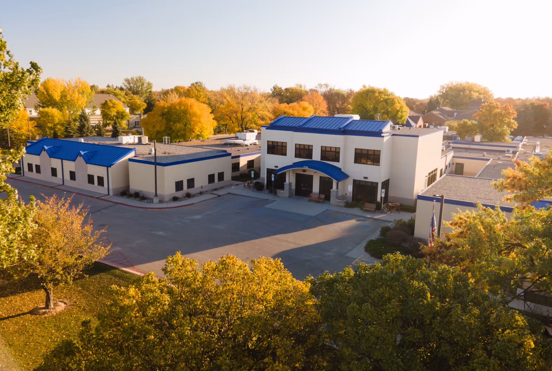 Aerial view of a white senior care complex with blue roofs and an entry courtyard surrounded by trees with autumn foliage.