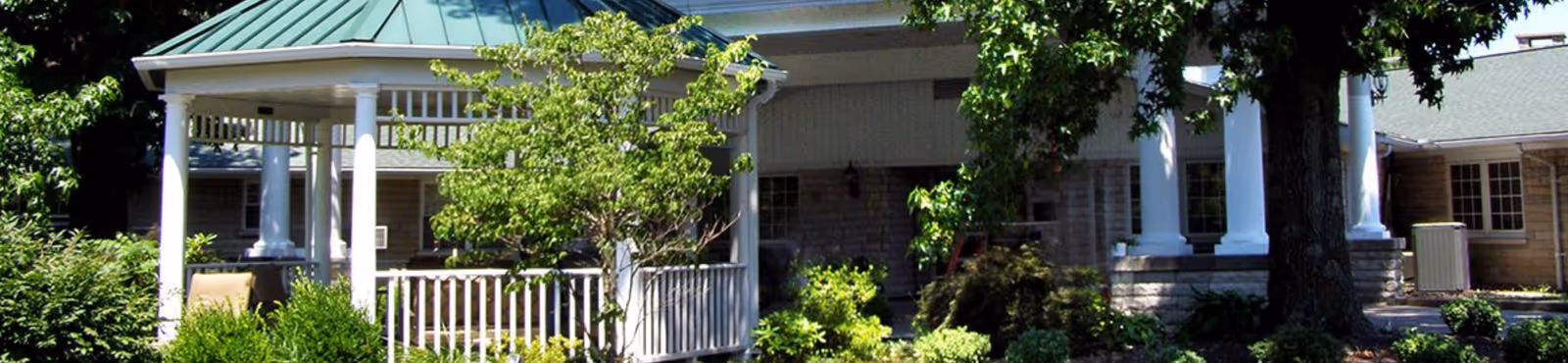 Front view of a building with a white-columned gazebo, green metal roof, and landscaped shrubs.