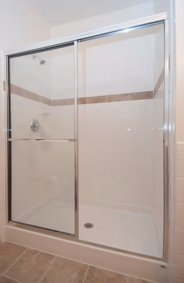 Tiled walk-in shower with sliding glass doors, chrome fixtures, and a horizontal decorative tile band.