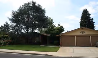 A single-story care home with a two-car garage, front lawn, and trees.