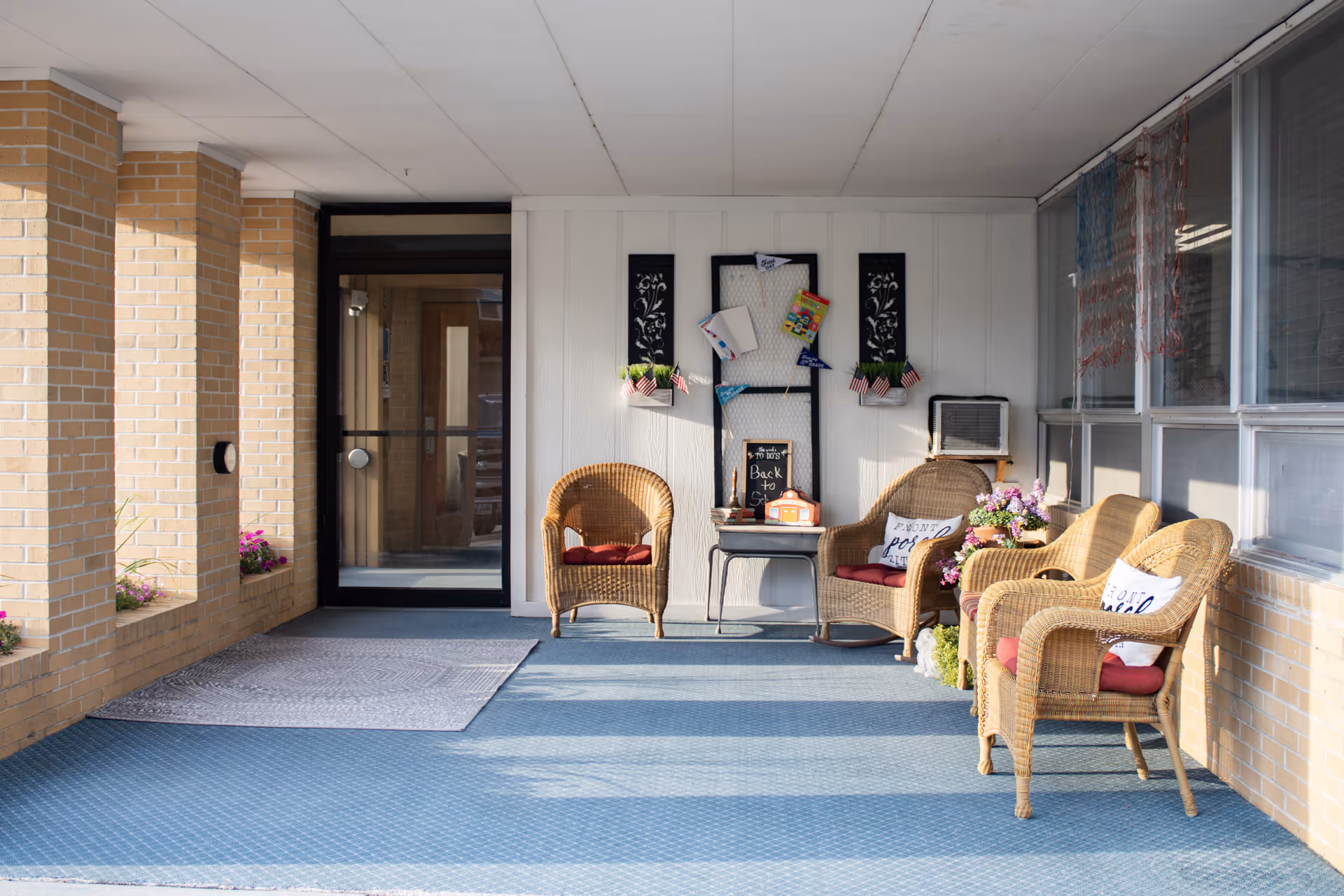 Covered entrance seating area with wicker chairs, cushions, and decorative wall hangings at the front of the facility.