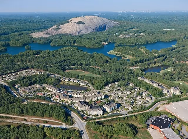 Aerial view of a residential complex set among trees and lakes with a large rocky hill in the background.