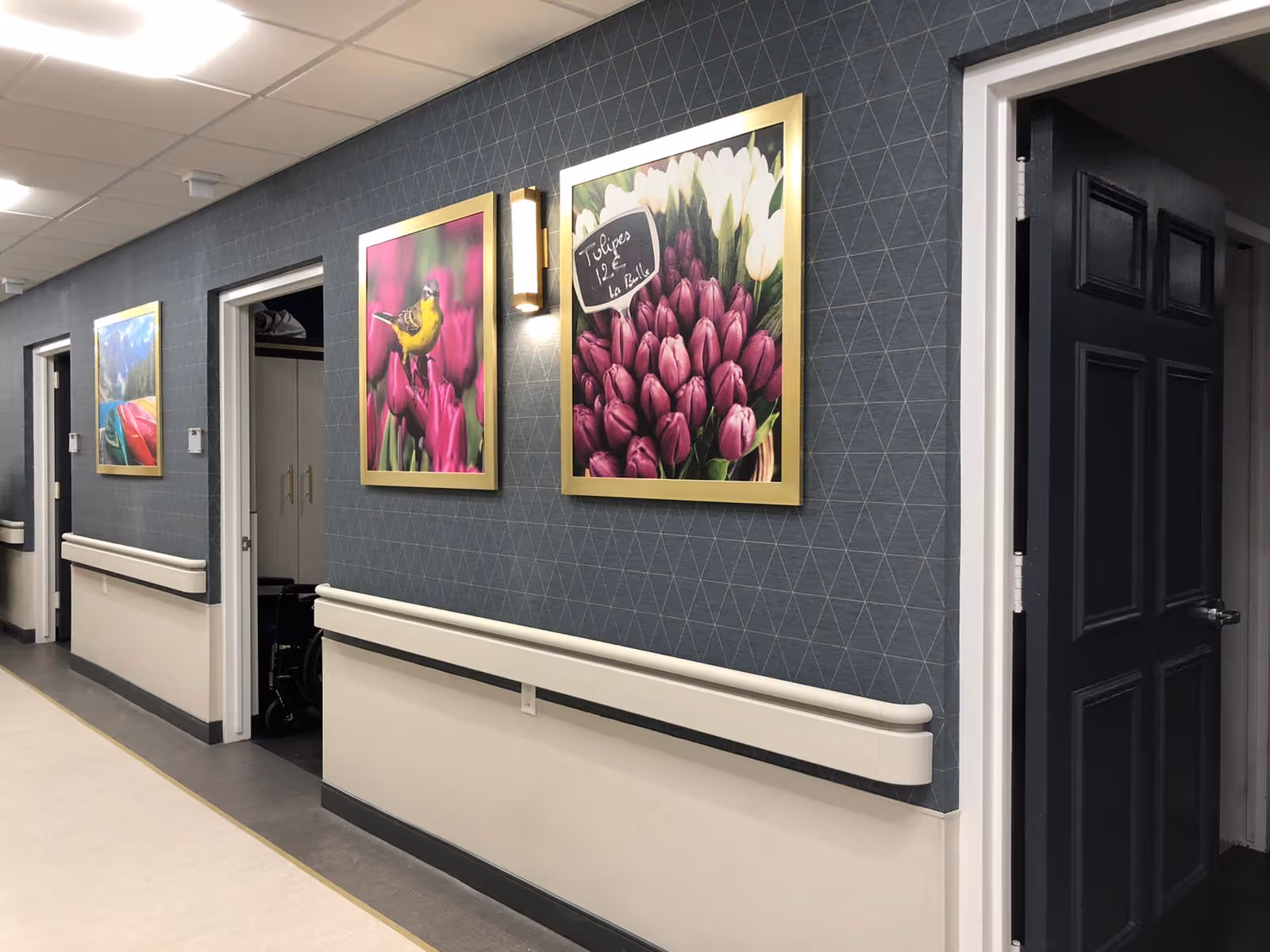 A decorated interior hallway with handrails and framed floral and bird artwork on the walls.