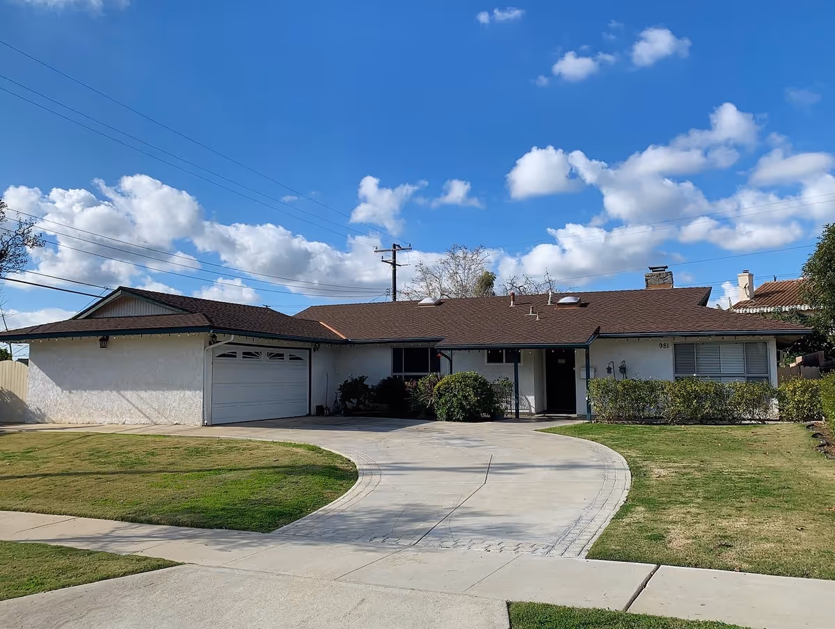 Single-story ranch-style house with an attached two-car garage, curved driveway and front lawn under a blue sky.